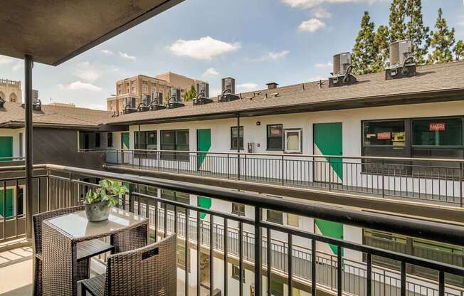 A balcony with a table and chairs overlooks a building with green and white doors.