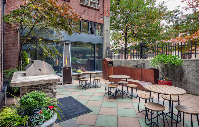A patio with tables and chairs is surrounded by trees.