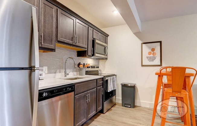 A kitchen with stainless steel appliances and wooden cabinets with an orange table and chairs.