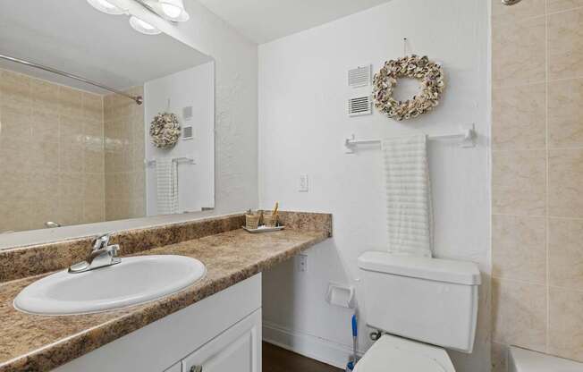 A bathroom with a toilet, sink, and a wreath on the wall.