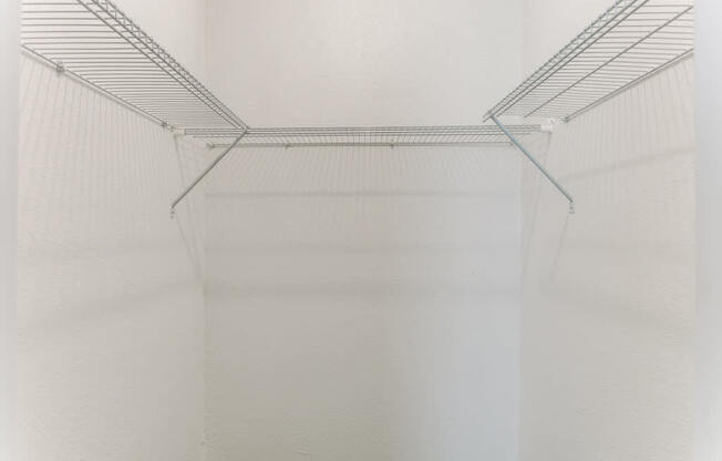 a walk in closet with white walls and a clear wire shelving system