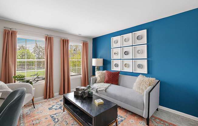 A living room with a grey couch, a coffee table, and a window with curtains.
