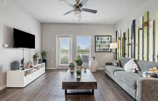 A living room with a grey couch, a wooden coffee table, a flat screen TV, and a ceiling fan.