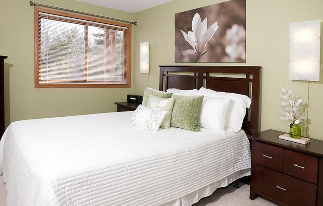 Bedroom with white comforter, decorative pillows, wooden headboard, and artwork of flowers hanging on the wall