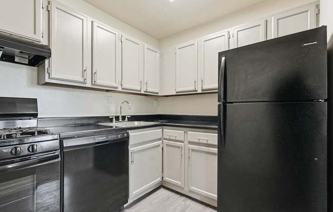 A black refrigerator stands in a kitchen with white cabinets.