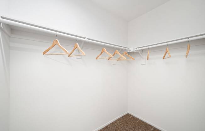 a walk in closet with white walls and wooden clothes hangers