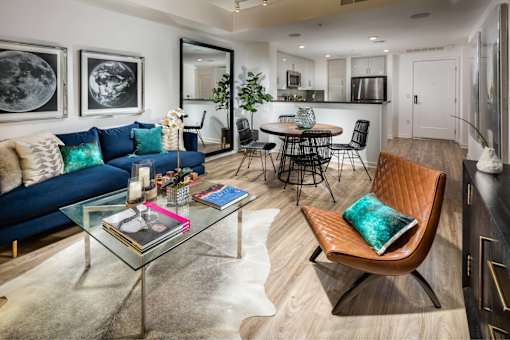 A modern living room with a blue sofa, a glass coffee table, and a brown leather chair.