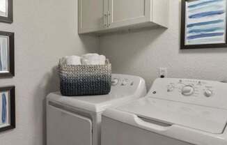 A white washing machine and dryer with a basket of towels on top of the washer.