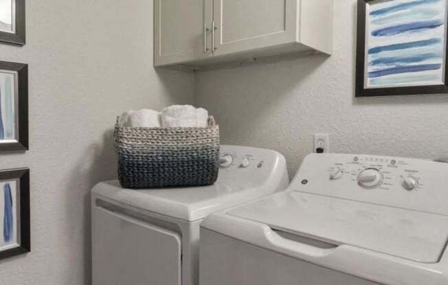 A white washing machine and dryer with a basket of towels on top of the washer.