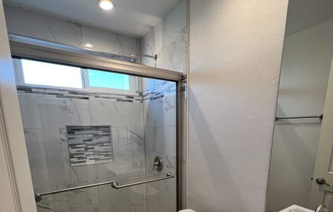 View of bathroom with walk in tile shower, well lit window above, toilet, and sink