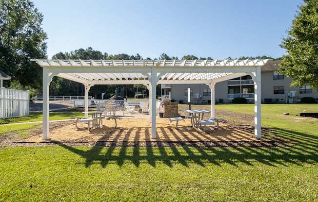 a white pergola with benches and tables in a park