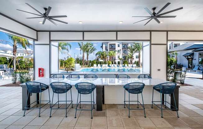 A patio with a bar and chairs overlooking a pool.