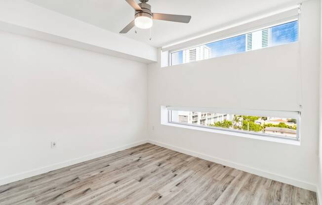 an empty room with a ceiling fan and two windows