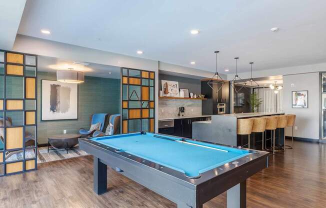 A pool table is in the middle of a room with a bar and a kitchen in the background.