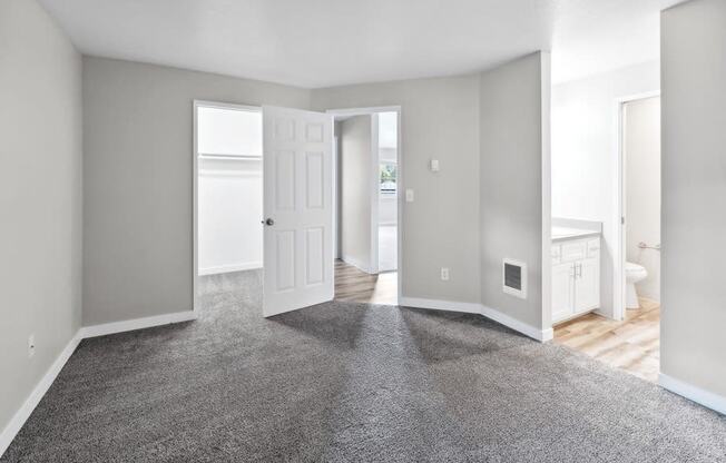 an empty living room with a carpeted floor and a door to a bathroom