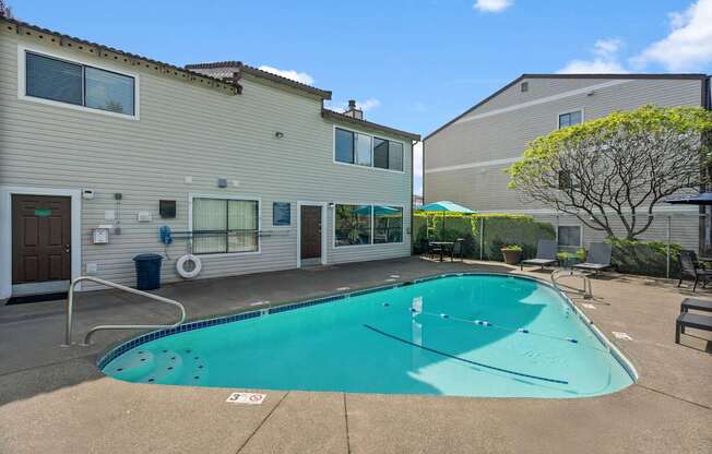 A swimming pool in front of a building with a tree to the right.