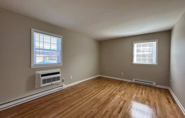 an empty living room with wood floors and a radiator and two windows