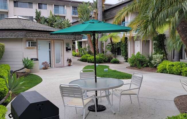 Umbrella table and chairs, barbeque, and leasing office in courtyard at La Mesa Village Apartments in La Mesa, California.