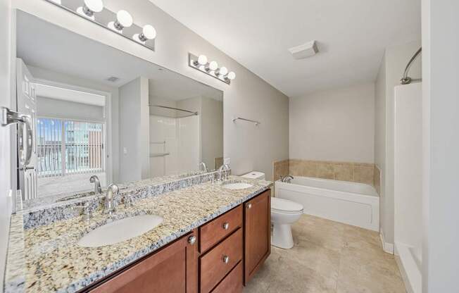 Apartment bathroom with dual-sink granite vanity, wood cabinetry and soaking tub