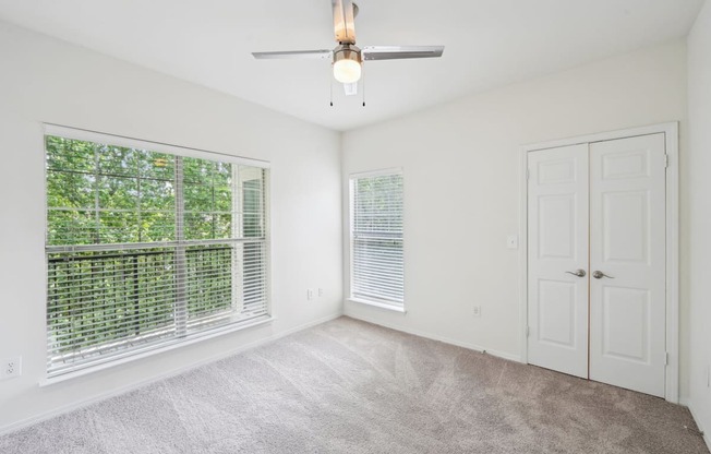 A room with a ceiling fan and two windows with blinds.
