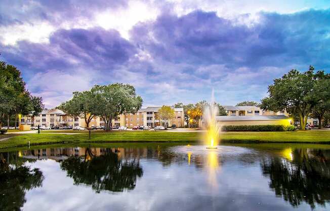A fountain in the middle of a pond in front of a building.