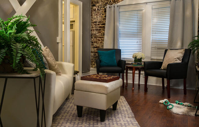 Pasadena Brookmore Suite with cream sofa, small sitting area by window, an open door to kitchen, and Exposed Brick Wall