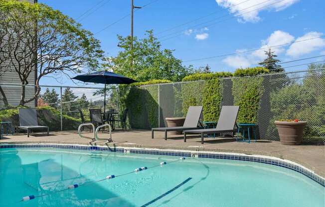 A pool with a diving board and lounge chairs.