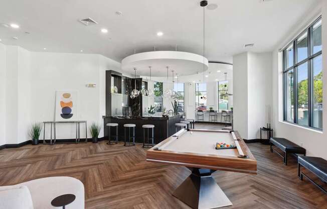 A billiard table is in the middle of a room with a white chair and a bar area.