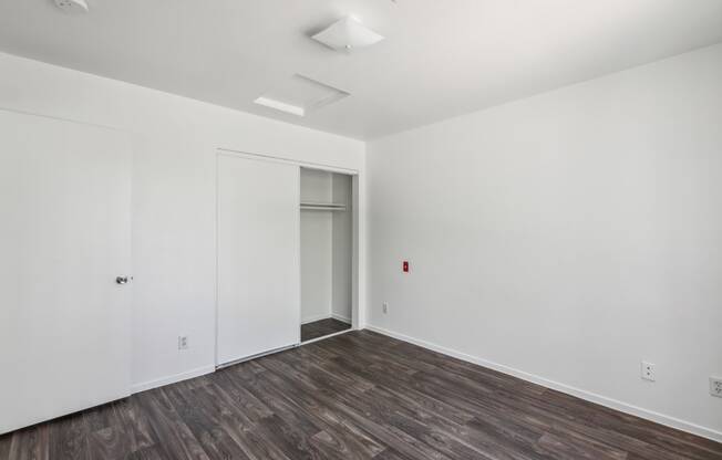 a bedroom with white walls and wood flooring and a closet