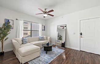 A living room with a beige couch, a blue rug, and a ceiling fan.