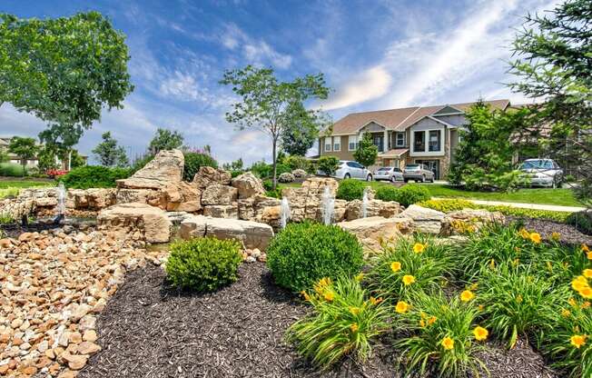 Riverstone - Landscaping with stone fountain, yellow flowers, trees, and shrubs