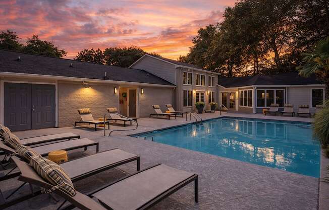 A poolside area with lounge chairs and a house in the background during sunset.