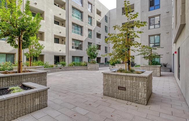Paved courtyard with raised planters, greenery, and firepits that create a calm outdoor space.