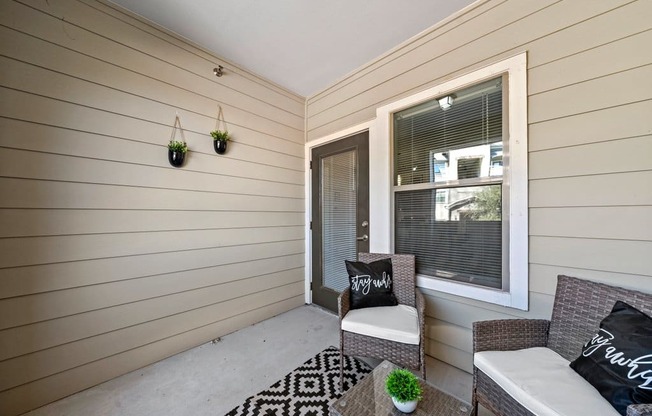 A small balcony with a couch, chair, and potted plant.