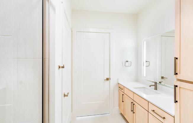 Primary bathroom with a double vanity, light wood cabinetry, integrated lighting, and a glass-enclosed shower arranged for daily routines.