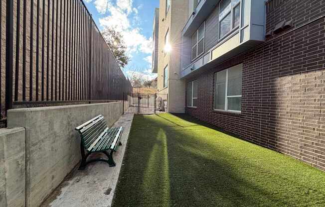 A green bench sits on a concrete path in front of a brick building.