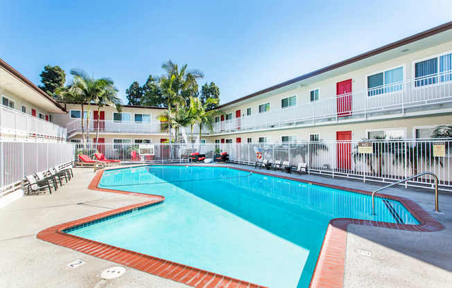 Outdoor swimming pool with sun chairs, a lounge area lined with apartments, and palm trees at Pacific Sands, San Diego, CA