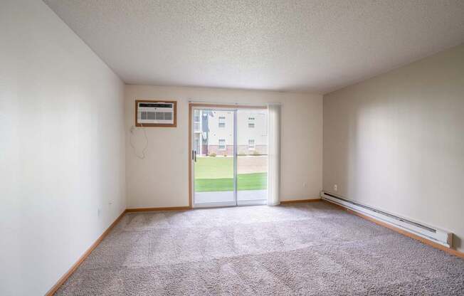 A room with a carpeted floor and a sliding glass door leading to a balcony. Fargo, ND Stonebridge Apartments