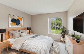 A bedroom with a large bed, a nightstand, and a window overlooking a green lawn.