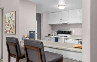 a kitchen with white cabinets and a counter with two chairs
