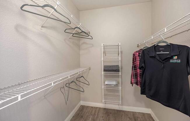 A black shirt with a logo is hanging on a hanger in a white closet.