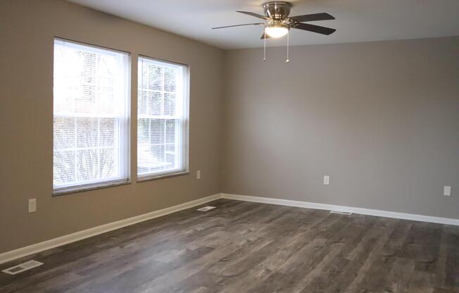 an empty living room with wood floors and a ceiling fan