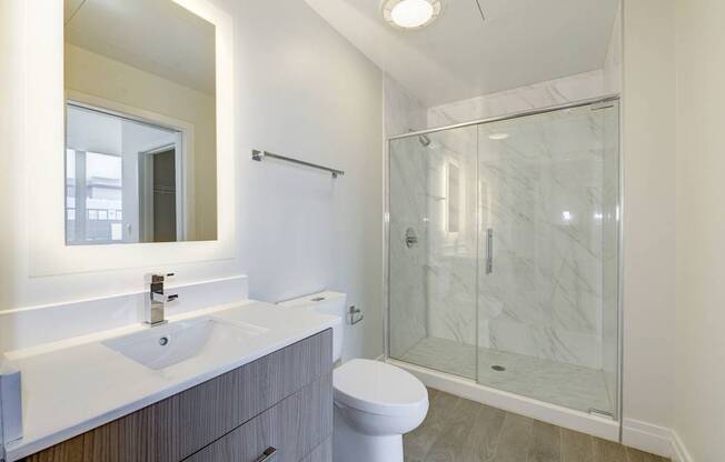 A bathroom with a toilet, sink, mirror, and shower.