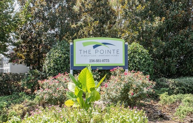 a sign for the pointe in a garden with bushes and trees