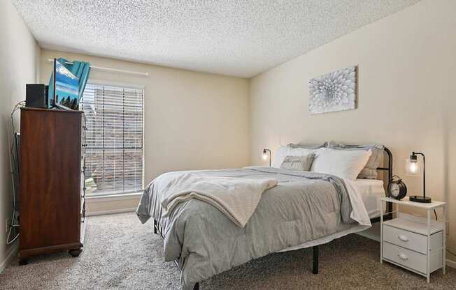 A bedroom with a bed, nightstand, and window with blinds.