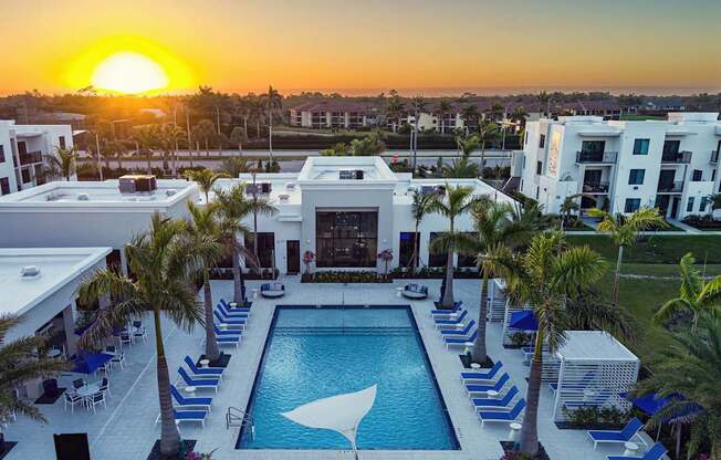 A sunset view of a pool area with lounge chairs and palm trees.
