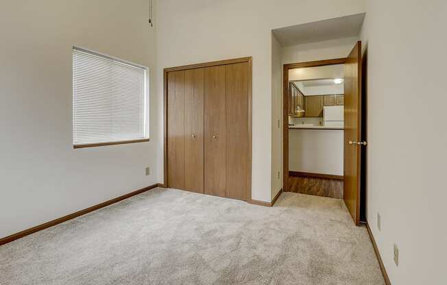 an empty living room with carpet and a door to a kitchen