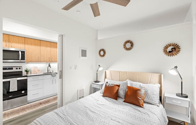 A bedroom with a large bed and a kitchen area in the background.