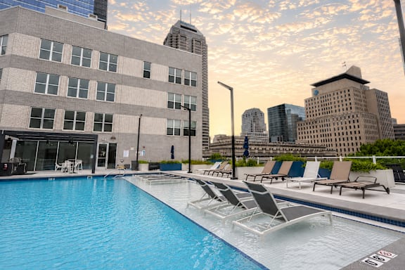 A swimming pool with lounge chairs and a city skyline in the background.