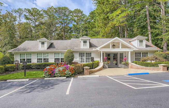 A large white building with a grey roof and a parking lot in front.